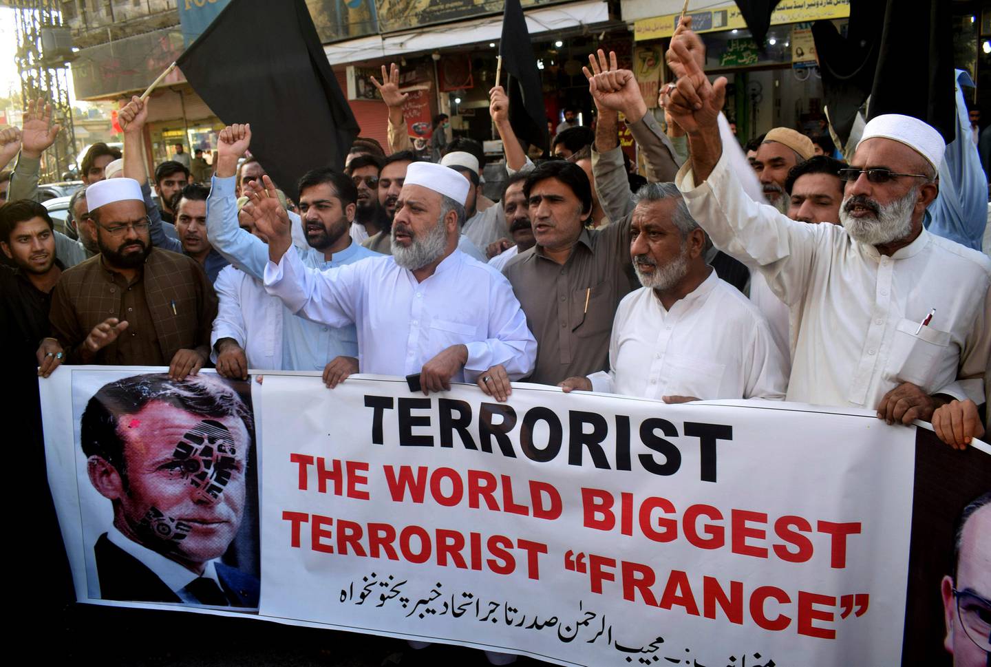 Pakistan traders hold a banner with a defaced picture of French President Emmanuel Macron during a protest against the publishing of caricatures of the Prophet Muhammad they deem blasphemous, in Peshawar, Pakistan, Monday, Oct. 26, 2020. Pakistan's Prime Minister Imran Khan said the French leader chose to encourage anti-Muslim sentiment and deliberately provoke Muslims by encouraging the display of blasphemous cartoons targeting Islam. (AP Photo/Muhammad Sajjad)
