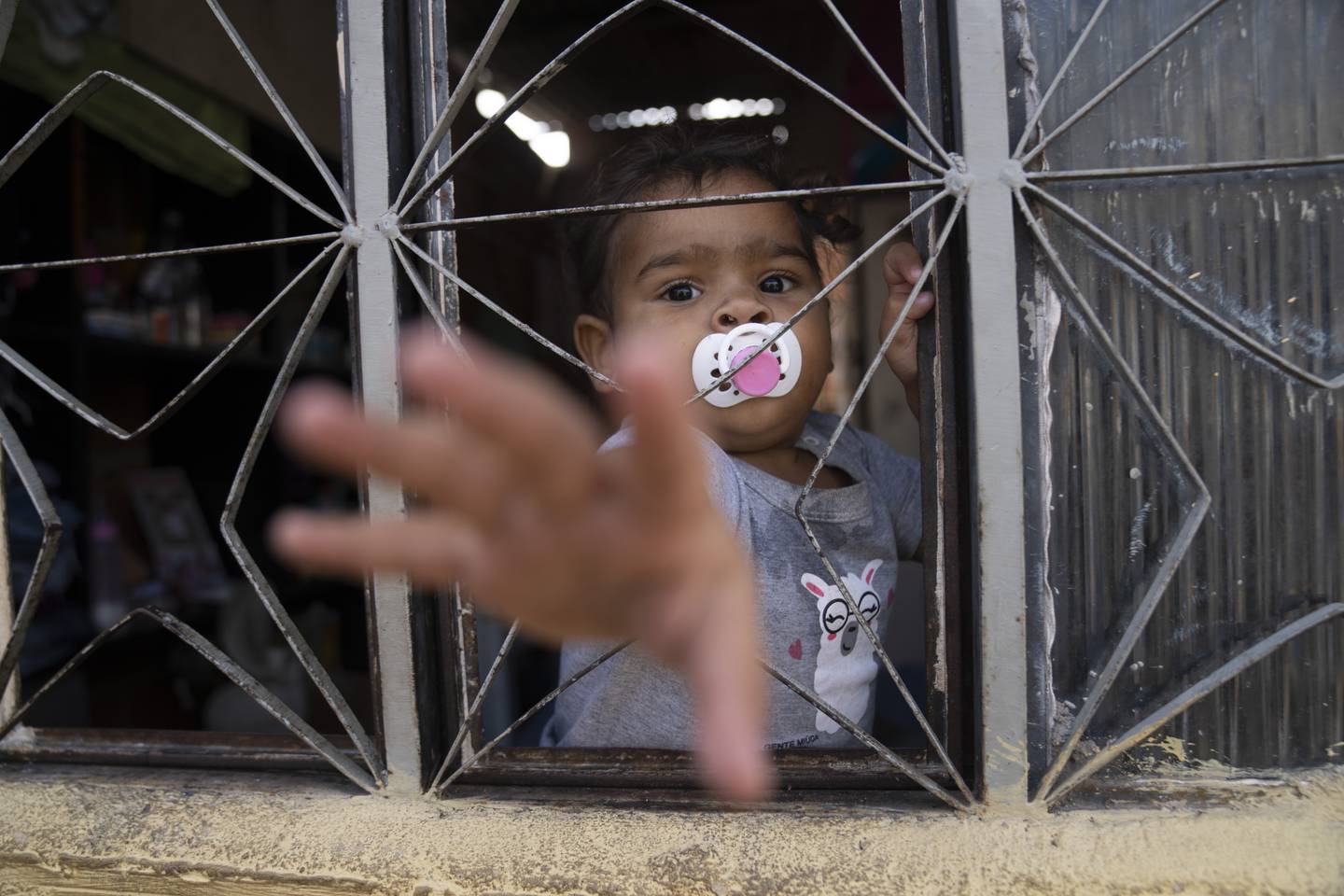 En jente stikker hånden ut av vinduet i et hjem bygget i et område som er okkupert av flere hundre fattige familier i Rio de Janeiro. Foto: Silvia Izquierdo / AP / NTB