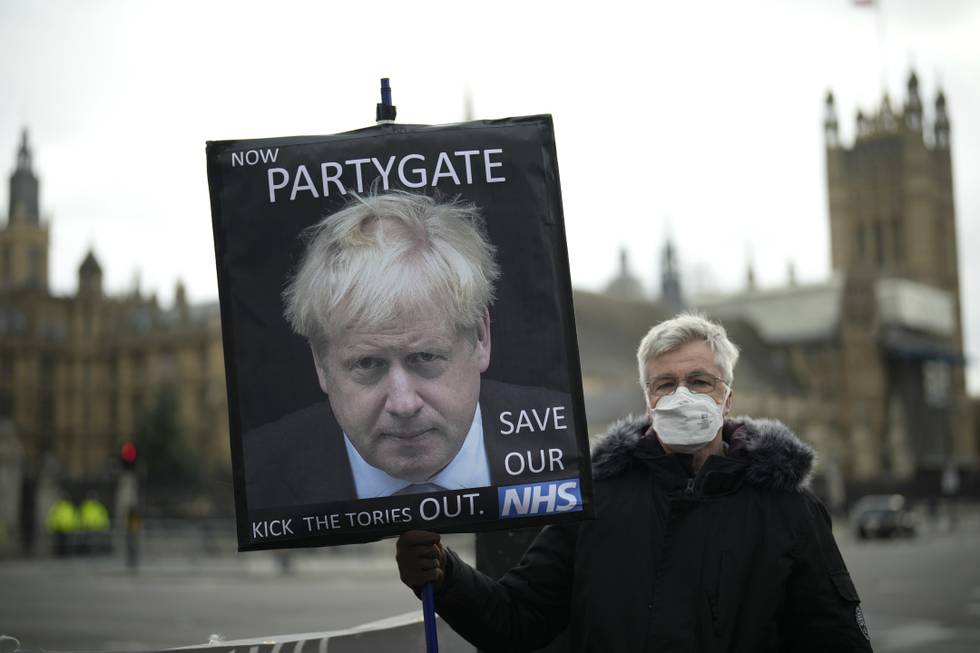 Bildet er av en demonstrant holder en plakat med bilde av Storbritannias statsminister Boris Johnson utenfor parlamentet. Bildet er fra det ble kjent at det skal ha vært mange ulovlige fester i statsministerboligen i Downing Street. Arkivfoto: Matt Dunham / AP / NTB