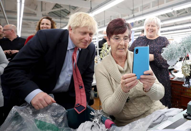 Britain's Prime Minister Boris Johnson poses for a selfie with a worker as he visits John Smedley Mill in Matlock, England, Thursday, Dec. 5, 2019. Britain is holding a general election a week from now and fractures are emerging within jittery political parties unsure how a volatile electorate will judge them. Conservative Prime Minister Boris Johnson and main opposition Labour Party leader Jeremy Corbyn both faced criticism of their moral character. (Hannah McKay/Pool Photo via AP)