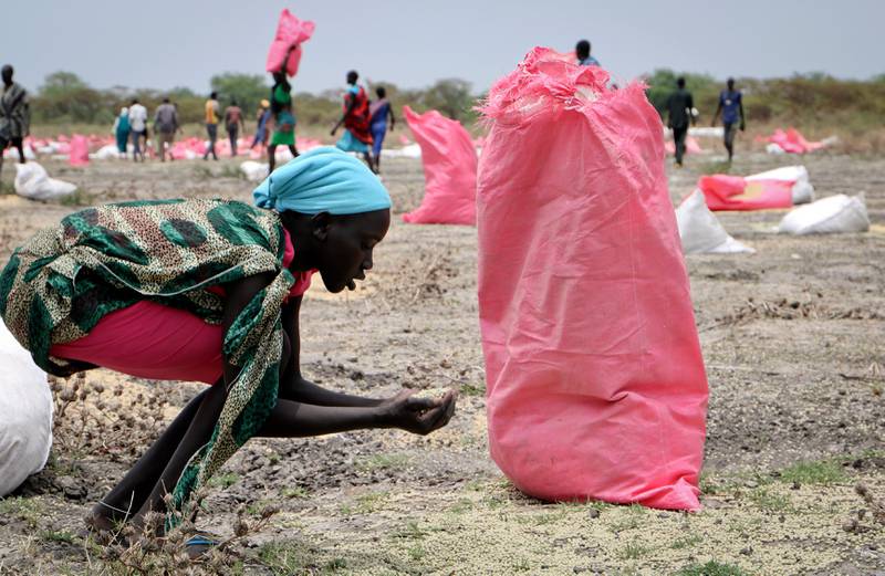 FILE - In this Wednesday, May 2, 2018 file photo, a woman scoops fallen sorghum grain off the ground after an aerial food drop by the World Food Programme (WFP) in the town of Kandak, South Sudan. An adviser to South Sudan's president said Thursday, Dec. 19, 2019 that the country is recalling its ambassador to the United States, in response to sanctions placed by the U.S. Treasury earlier this week on two senior South Sudanese officials. (AP Photo/Sam Mednick, File)