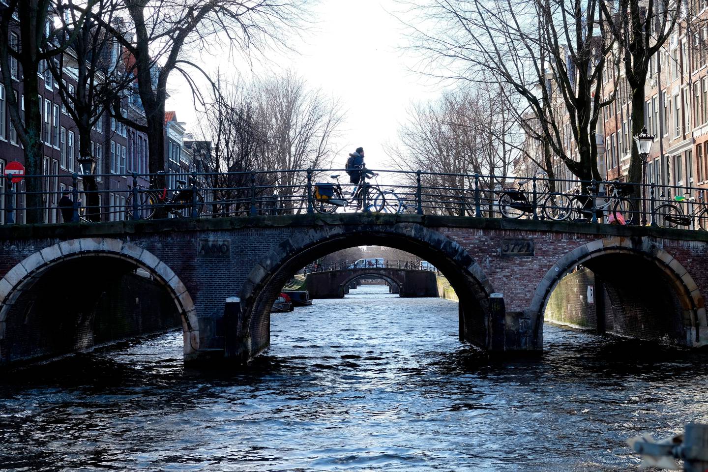 A cyclist pedals over a bridge over the Leidsegracht canal in Amsterdam, Thursday, Feb. 7, 2019.  Amsterdam's city hall says that kilometers (miles) of walls along its world famous canals are crumbling and in urgent need of repair following years of neglect. (AP Photo/Michael Corder)