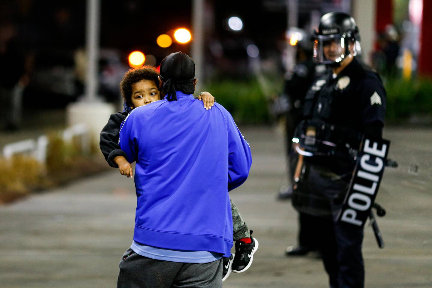 A man holding a child walks by police officers during a protest on election night, Tuesday, Nov. 3, 2020, in Los Angeles. (AP Photo/Ringo H.W. Chiu)