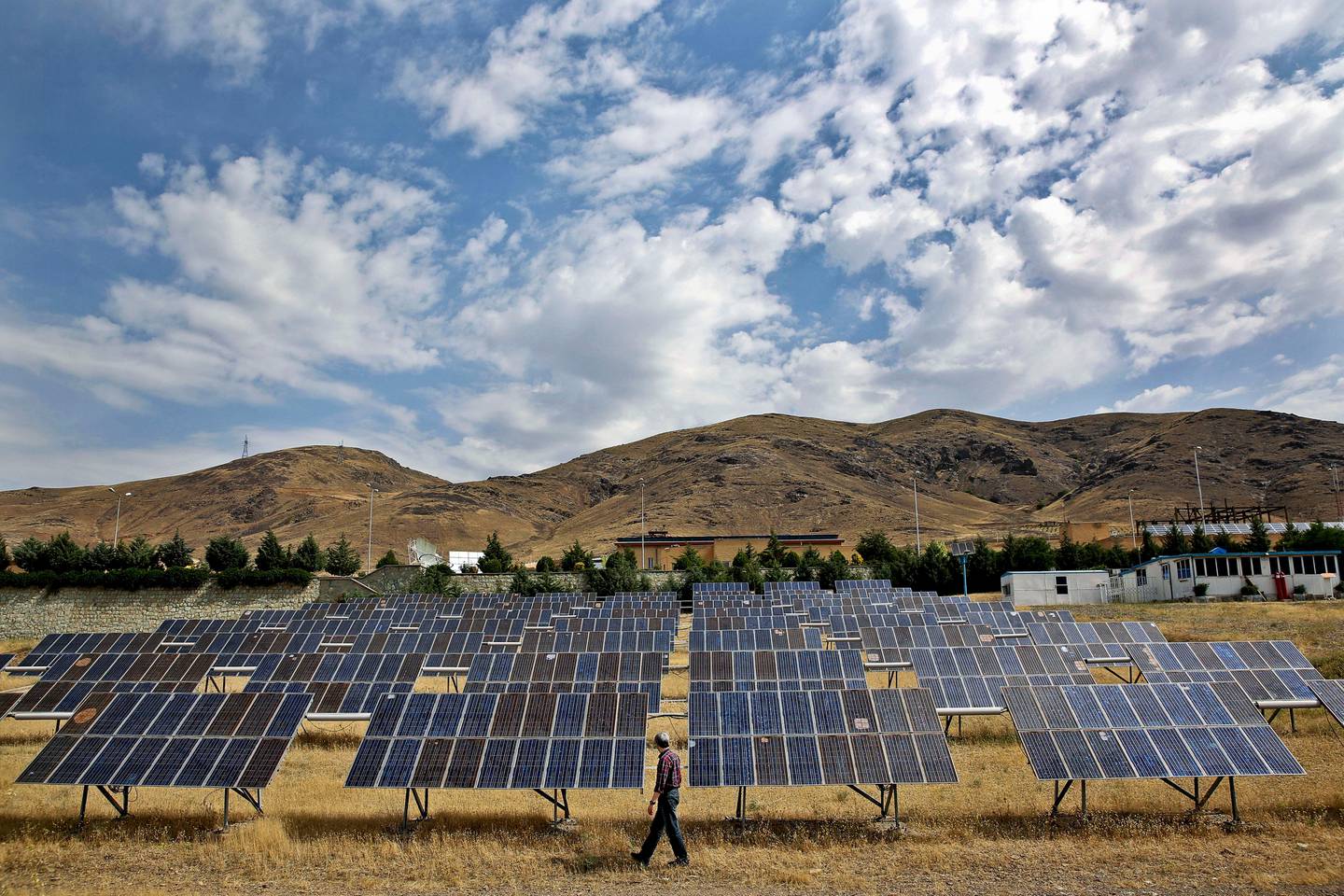 In this June, 22, 2014 photo, a man looks at solar panels at the Taleghan Renewable Energy Site in Taleghan, 160 kilometers (99 miles) northwest of capital Tehran, Iran. President Hassan Rouhani?s government has quintupled its spending on solar power projects in the last year, taking advantage of Iran?s 300-odd days of sunshine a year that make its vast sun-kissed lands one of the best spots on earth to host solar panels. While being good for the environment, the panels also offer rural Iran steady power amid uncertainty over the country?s contested nuclear program as it negotiates with world powers. (AP Photo/Ebrahim Noroozi)