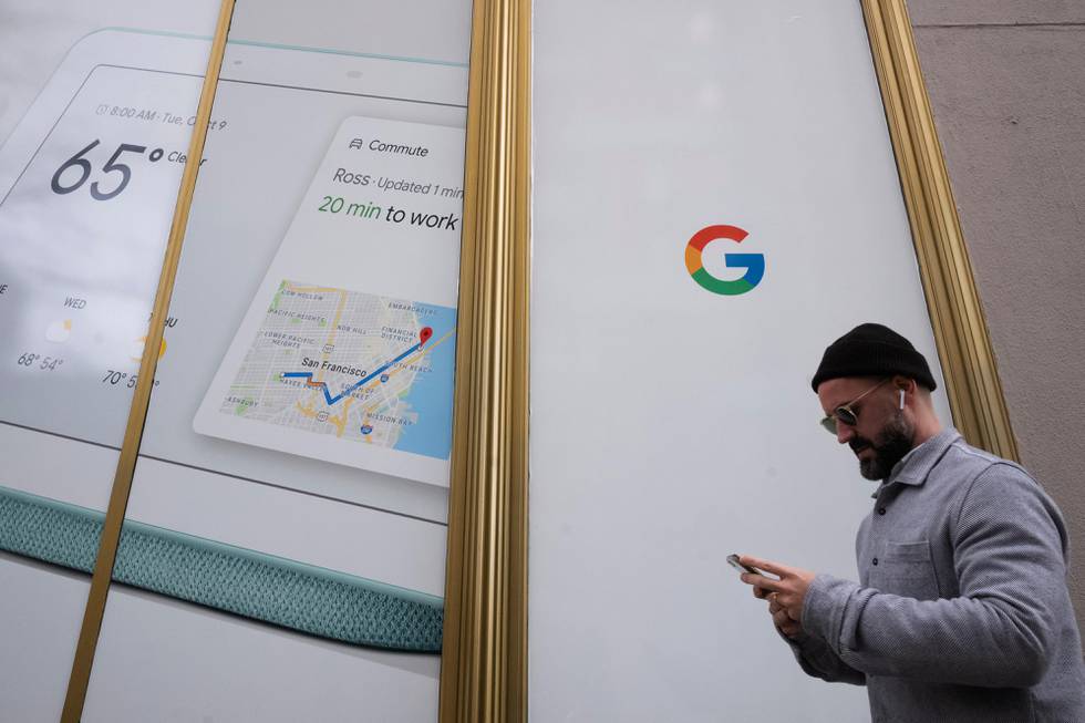 FILE- In this Dec. 17, 2018, file photo a man using a mobile phone walks past Google offices in New York. Alphabet Inc., parent company of Google, reports financial results on Monday, Feb. 4, 2019. (AP Photo/Mark Lennihan, File)