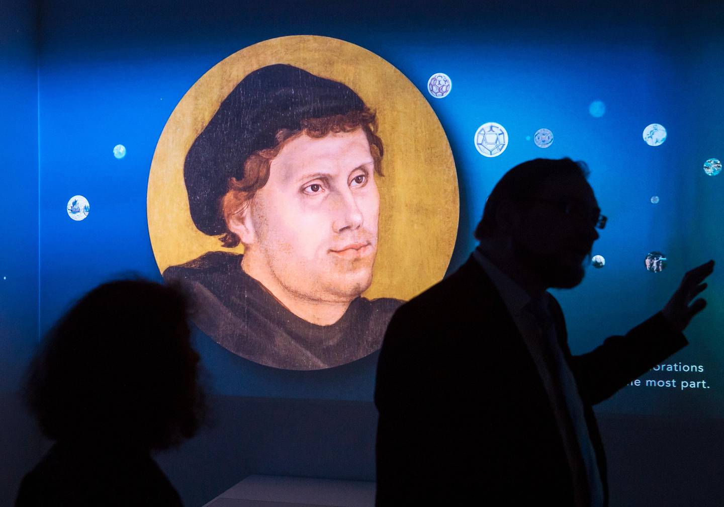 Visitors stand in front of a video installation displaying a portrait of Martin Luther during the press preview of the exhibition '95 Treasures ?Äì 95 People' in the Augusteum in Wittenberg, Germany, Friday, May 12, 2017. The focus of the exhibition is on Luther's nailing of the theses on the door of the Castle Church. The exhibition starts on May 13, 2017 and lasts until Nov. 5, 2017. (AP Photo/Jens Meyer)