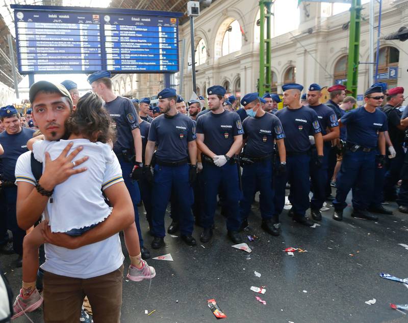 En ung mann bærer barnet sitt framfor ungarsk politi, som holder vakt ved togstasjonen i Budapest tirsdag. 