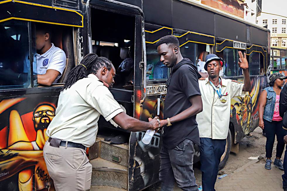 A bus conductor disinfects the hands of a passenger, after the government directed all operators of "matatus", or public minibuses, to provide hand sanitizer to their clients, on a busy street in downtown Nairobi, Kenya Friday, March 13, 2020. Authorities in Kenya said Friday that a Kenyan woman who recently traveled from the United States via London has tested positive for the new coronavirus, the first case in the East African country. (AP Photo/Patrick Ngugi)