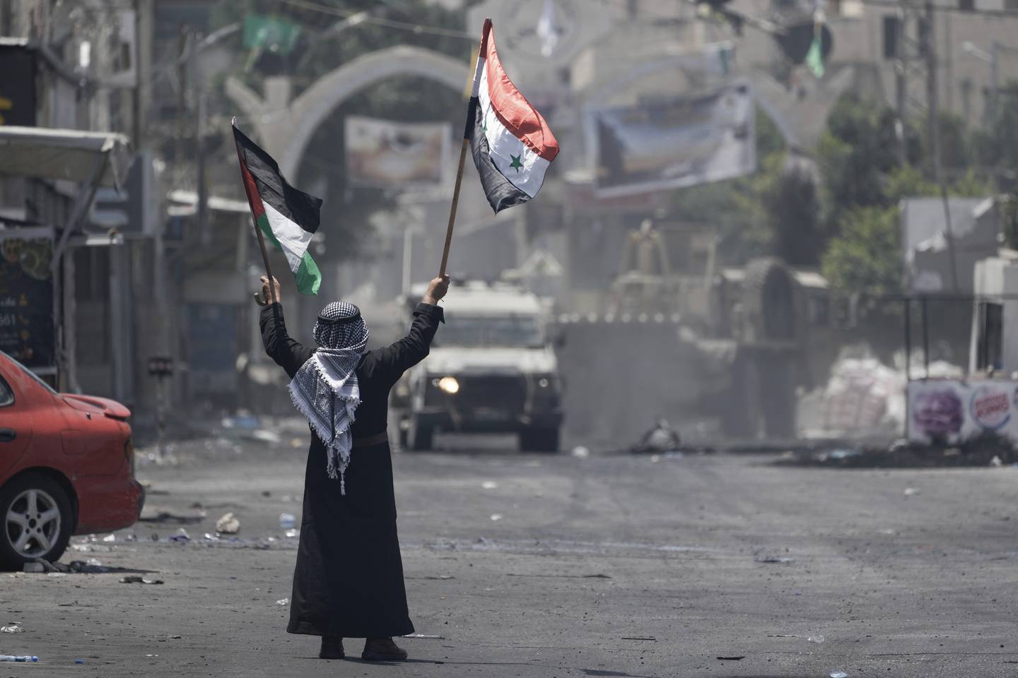 En palestinsk mann vifter med et palestinsk og et syrisk flagg foran et israelsk militærkjøretøy i den okkuperte palestinske flyktningleiren Jenin tirsdag. Foto: Majdi Mohammed / AP / NTB