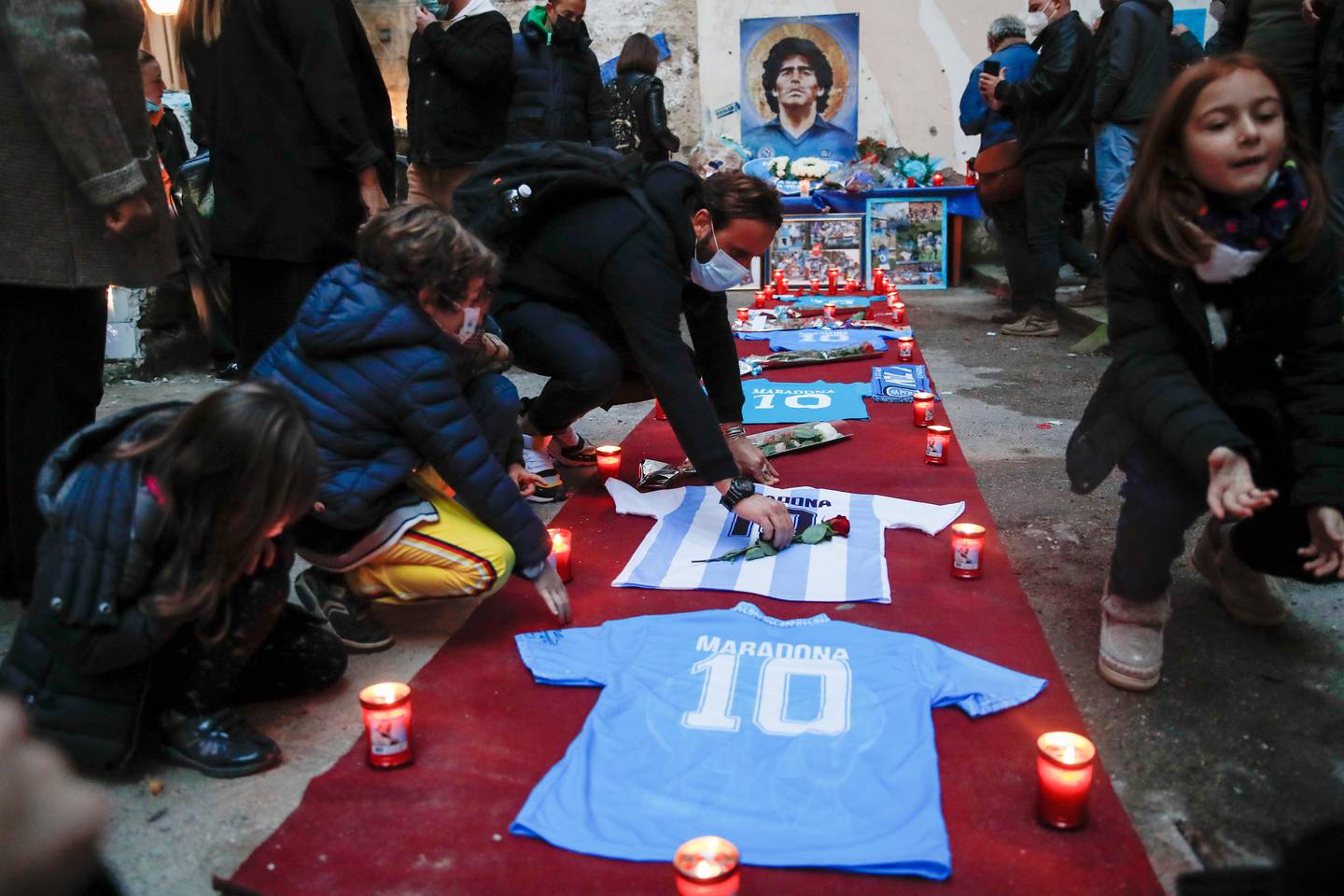 People gather and light candles to honor soccer legend Diego Maradona, at the popular "Quartieri Spagnoli" neighborhood, in Naples, Thursday, Nov. 26, 2020. Maradona died on Wednesday at the age of 60 of a heart attack in a house outside Buenos Aires where he recovered from a brain operation. (AP Photo/Alessandra Tarantino)