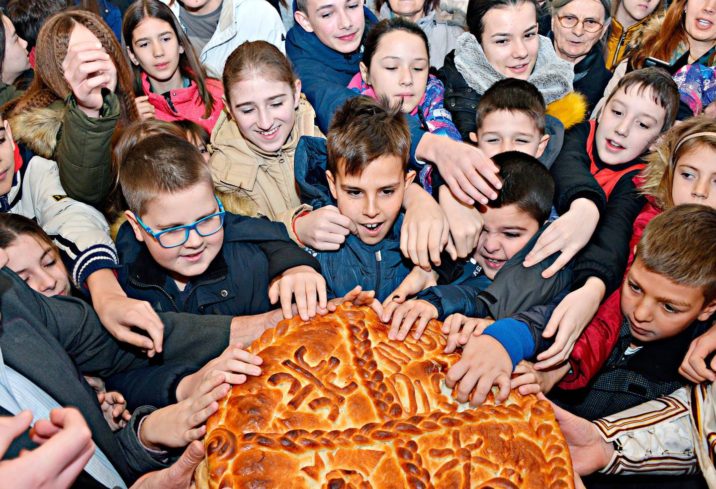 Children break the traditional Christmas bread to mark the Orthodox Christmas Day festivities in Banja Luka, Bosnia, Tuesday, Jan. 7, 2020. Children traditionally scramble for a piece of the bread, searching for a gold coin, hidden inside. (AP Photo/Radivoje Pavicic)