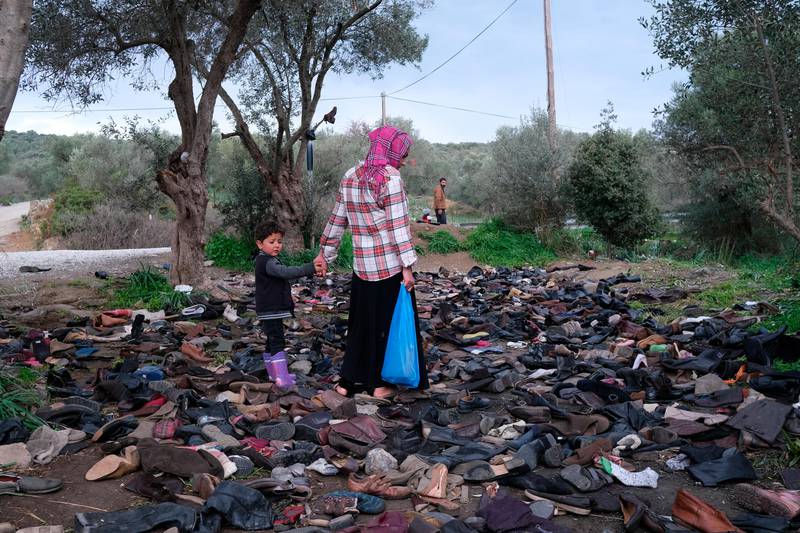 Migrants walk next to discarded shoes and boots outside the perimeter of the overcrowded Moria refugee camp on the northeastern Aegean island of Lesbos, Greece, Wednesday, March 11, 2020. Camps on Lesbos and other islands of the eastern Aegean are already overcrowded and operating above their capacity. (AP Photo/Aggelos Barai)
