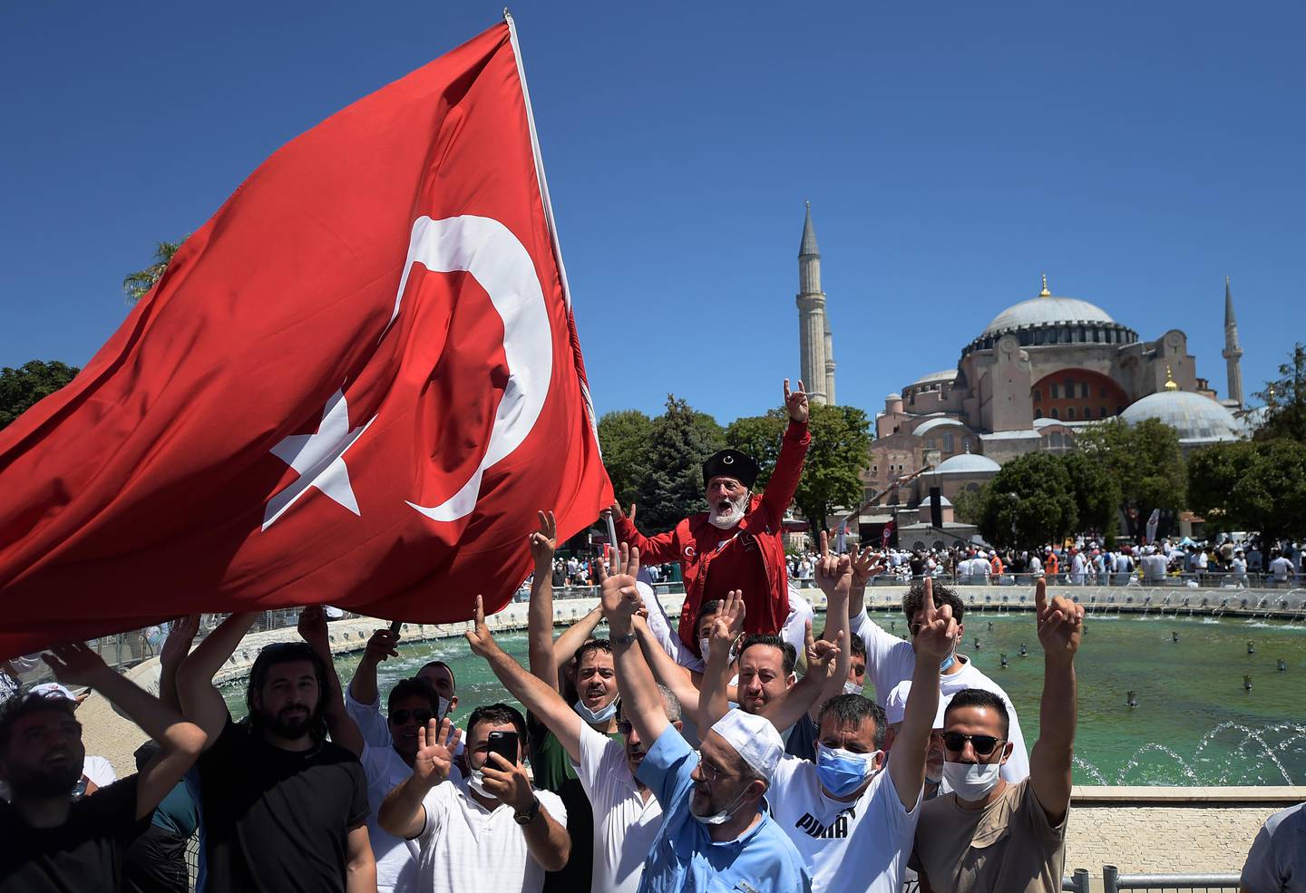 Faithful, one holding a Turkish flag, chant slogans as they wait at the historic Sultanahmet district of Istanbul, outside the Byzantine-era Hagia Sophia, Friday, July 24, 2020. Hundreds of Muslim faithful were making their way to Istanbul's landmark monument Friday to take part in the first prayers in 86 years at the structure that was once Christendom's most significant cathedral and the "jewel" of the Byzantine Empire then a mosque and museum before its re-conversion into a Muslim place of worship. The conversion of the edifice, has led to an international outcry. (AP Photo/Yasin Akgul)