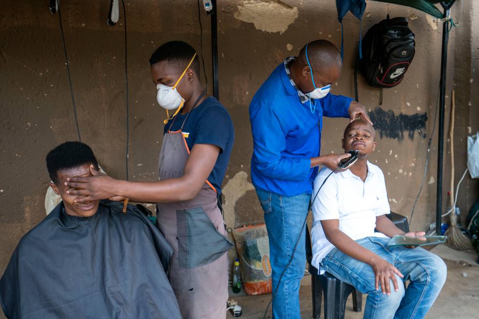 Barbers wearing protective masks attend to customers in the township of Soweto, outside Johannesburg, South Africa, Wednesday March 25, 2020. South Africa will go into a nationwide lockdown for 21 days starting Friday morning, in an effort to mitigate the spread to the coronavirus. The new coronavirus causes mild or moderate symptoms for most people, but for some, especially older adults and people with existing health problems, it can cause more severe illness or death.(AP Photo/Jerome Delay)