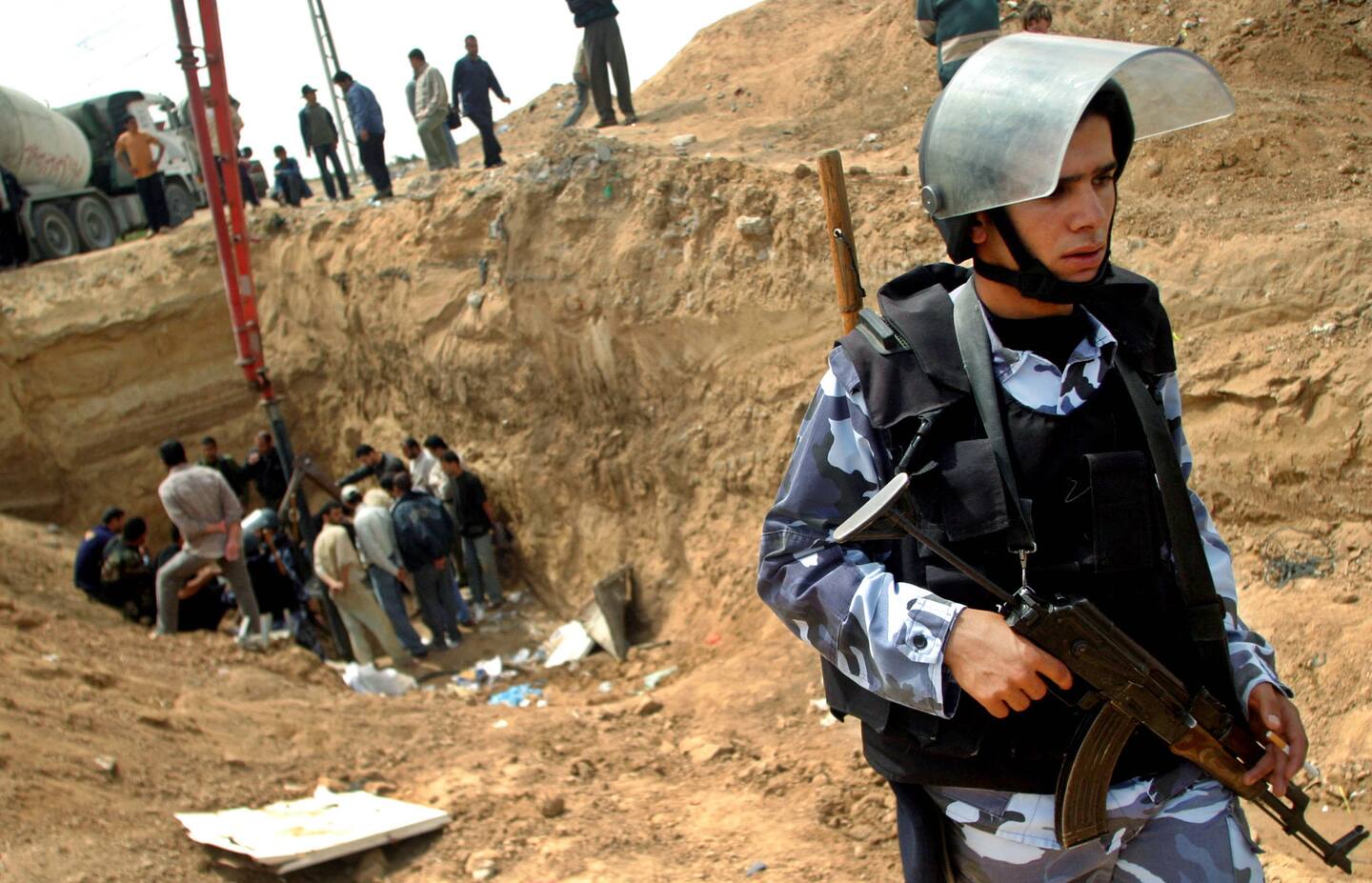 A Palestinian police officer stands guard as officers and workers, background, seal off a smuggling tunnel that was discovered next to the border with Egypt in the Rafah refugee camp, southern Gaza Strip, Sunday, April. 24.2005. The Palestinian Authority is under pressure from Israeli authorities, who say the tunnels are used to smuggle weapons into the Gaza Strip from neighboring Egypt. (AP Photo/Khalil Hamra)