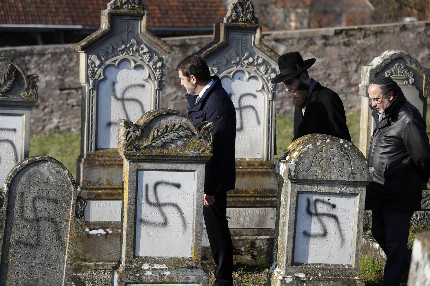 French Interior Minister Christophe Castaner, center, followed by Strasbourg chief Rabbi Harold Abraham Weill, second right, walk amid vandalized tombs in the Jewish cemetery of Westhoffen, west of the city of Strasbourg, eastern France, Wednesday, Dec. 4, 2019. Regional authorities in eastern France say vandals have scrawled anti-Semitic inscriptions, including swastikas spray-painted in black, on 107 tombs in a Jewish cemetery. (AP Photo/Jean-Francois Badias)