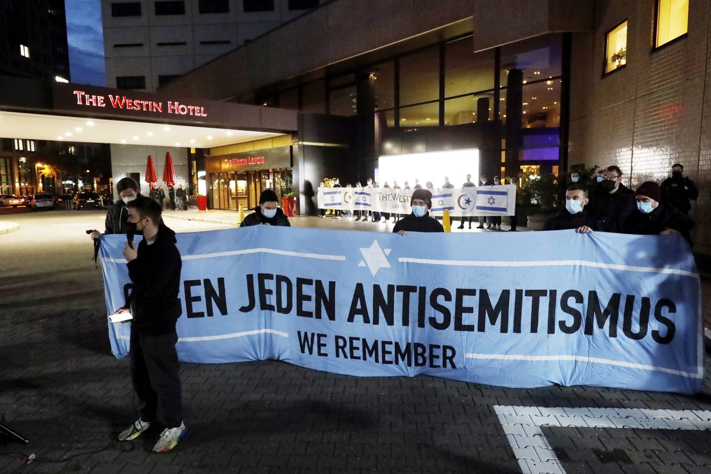 People gather in front of the "Westin Hotel" in Leipzig, Germany, Tuesday, Oct. 5, 2021 to show solidarity with the musician Gil Ofarim. A leading Jewish group in Germany says it's shocked by a German-Israeli singers report of being turned away from a hotel because he was wearing a Star of David pendant. Singer Gil Ofarim, who lives in Germany, shared a video on Instagram Tuesday showing him in front of the Westin hotel in Leipzig and saying a hotel employee asked him to put away his necklace in order to check in. (Dirk Knofe/dpa via AP)