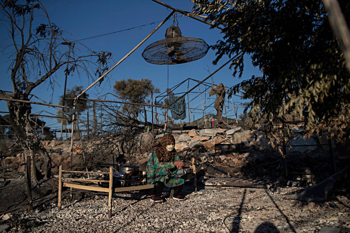 A migrant woman sits on a burned bed in the Moria refugee camp on the northeastern island of Lesbos, Greece, Thursday, Sept. 10, 2020. A second fire in Greece's notoriously overcrowded Moria refugee camp destroyed nearly everything that had been spared in the original blaze, Greece's migration ministry said Thursday, leaving thousands more people in need of emergency housing. (AP Photo/Petros Giannakouris)