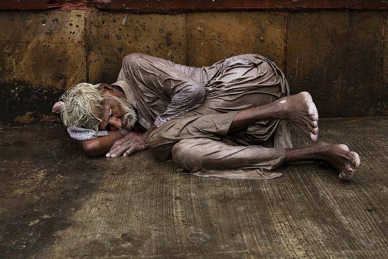 En hjemløs inder prøver å finne ly inntil en husvegg på en regnvåt gate i New Dehli. India har sterk økonomisk vekst, men ekstrem ulikhet bidrar til at nær 200 millioner indere er underernærte.