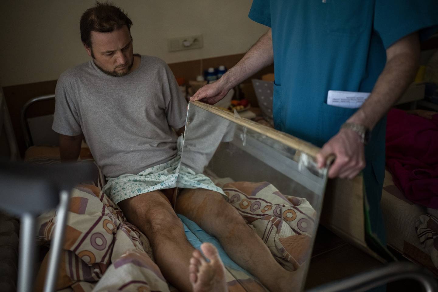 Sasha Horokhivskyi, 38, performs mirror therapy to mitigate phantom pains at a public hospital in Kyiv, Ukraine, Thursday, April 28, 2022. Sasha lost his leg above the knee on March 22 after being shot in the calf by a territorial defense member who mistook him for a spy after he stopped to take photos of bombed buildings near his home.(AP Photo/Emilio Morenatti)