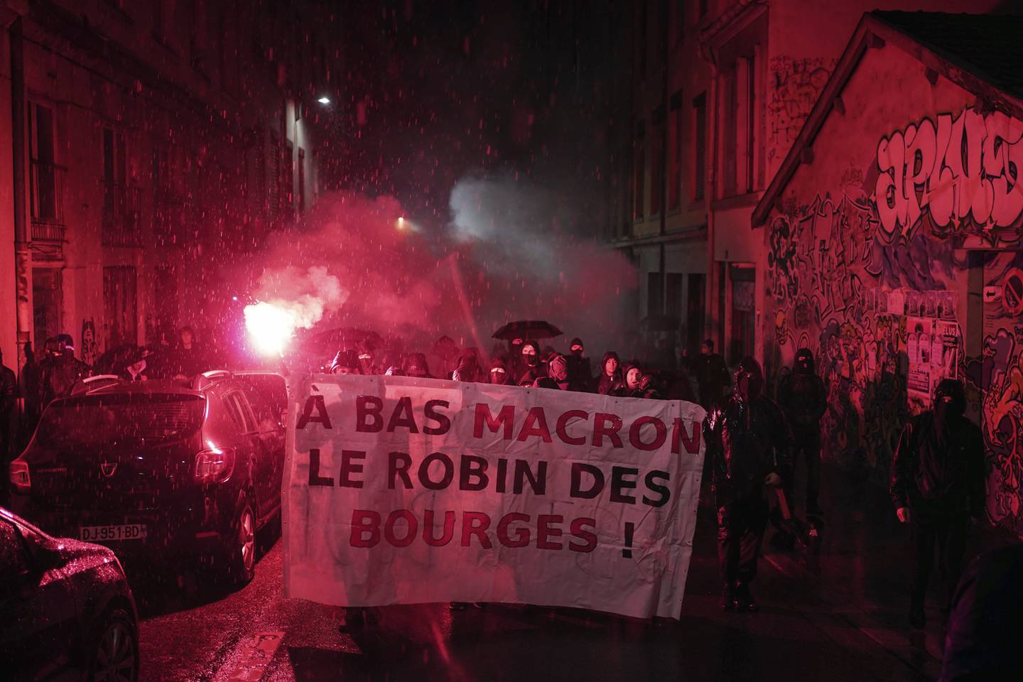 Maskekledde demonstranter med slagord rettet mot Frankrikes gjenvalgte president Emmanuel Macron ble møtt med tåregass av politiet i Lyon søndag. Foto: Laurent Cipriani / AP / NTB