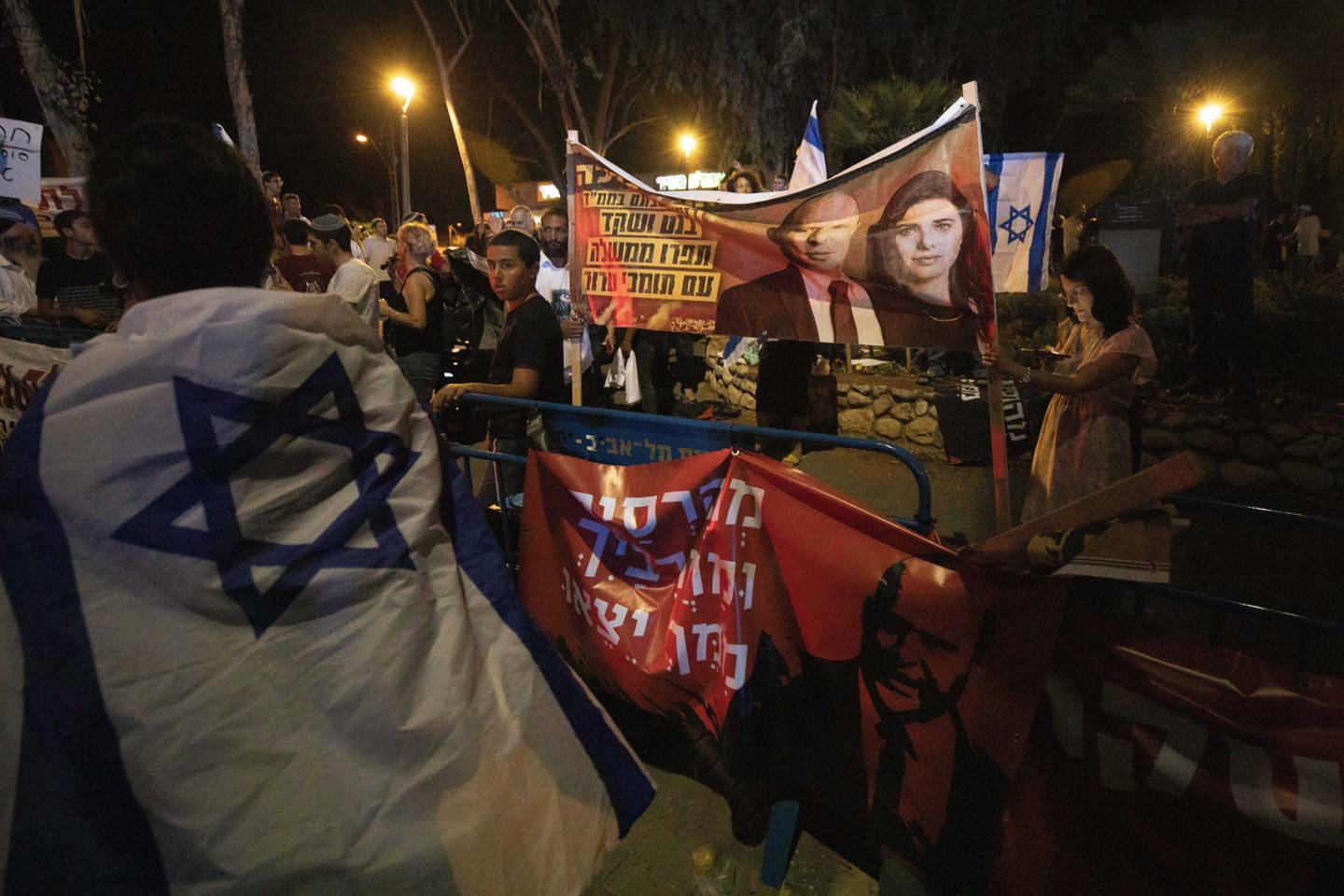 Israeli right-wing activists hold signs showing Naftali Bennett and Ayelet Shaked of the Yamina party, during a demonstration against the possibility of forming a new government in Tel Aviv, Israel, Sunday, May 30, 2021. Bennett, leader of the Yamina party and former ally of Prime Minister Benjamin Netanyahu on Sunday said he would seek to form a coalition government with the Israeli leader's opponents, taking a major step toward ending the rule of the longtime premier. (AP Photo/Sebastian Scheiner)